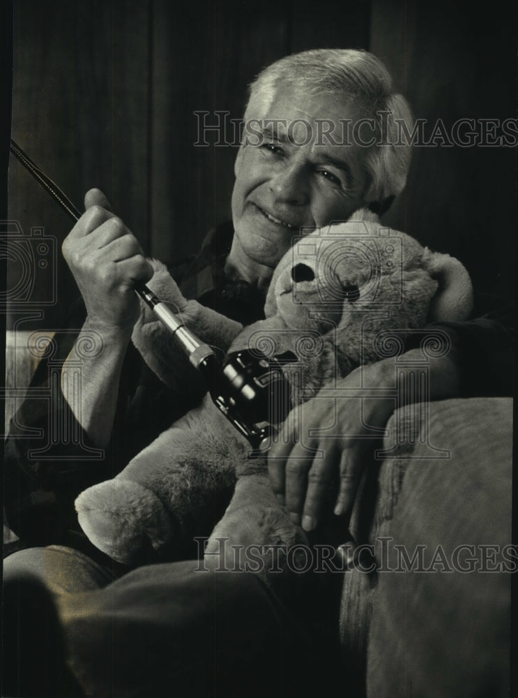 1993 Man cuddles stuffed toy animal and fishing rod - Historic Images