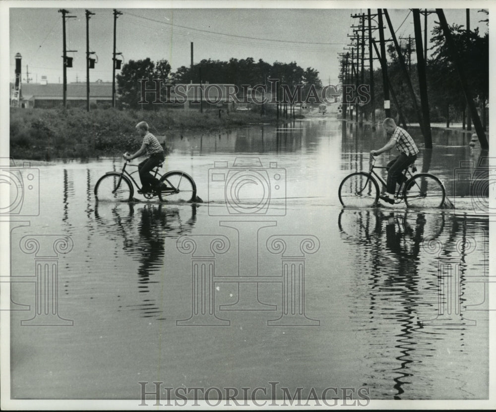 1969, Robert Brzycki and James Hintz ride through Milwaukee puddles - Historic Images