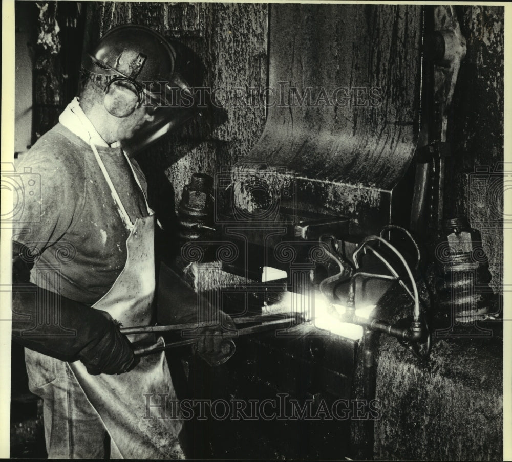 1980 Press Photo Joseph Gottweiss, uses tongs to hold hot steel under hammer - Historic Images