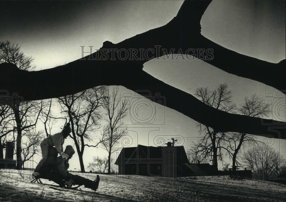 1989 Three children enjoy sledding on a hill in Milwaukee. - Historic Images