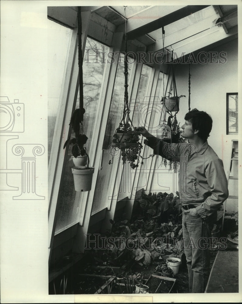 1979, Elmer Harris checks the moisture in a hanging planter in Chetek - Historic Images