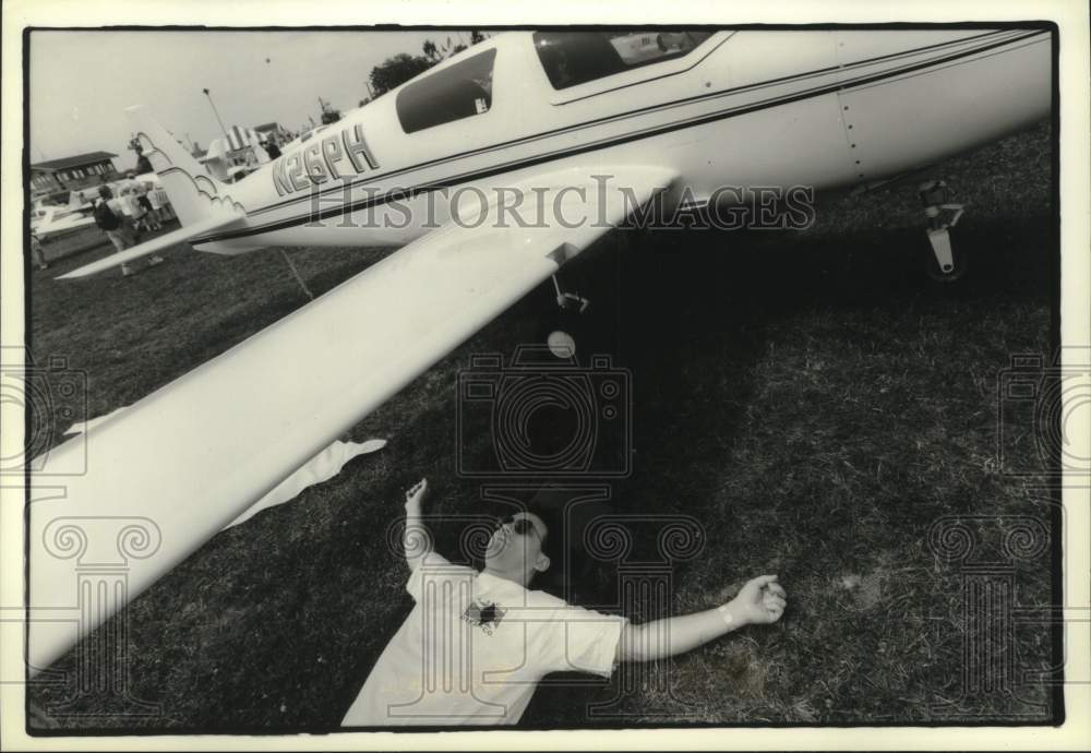 1994 Press Photo Bart Cleary rests in shade of plane wing at Wittman Airport - Historic Images