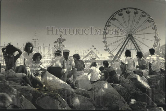 1989 Press Photo Crowds at Summerfest sit on rocks along Lake Michigan shore. - Historic Images