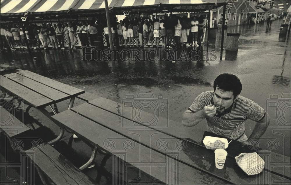 1987 Press Photo Lonely patron eats in the rain at Summerfest in Wisconsin. - Historic Images