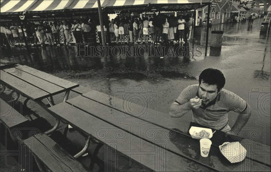 1987 Press Photo Lonely patron eats in the rain at Summerfest in Wisconsin. - Historic Images