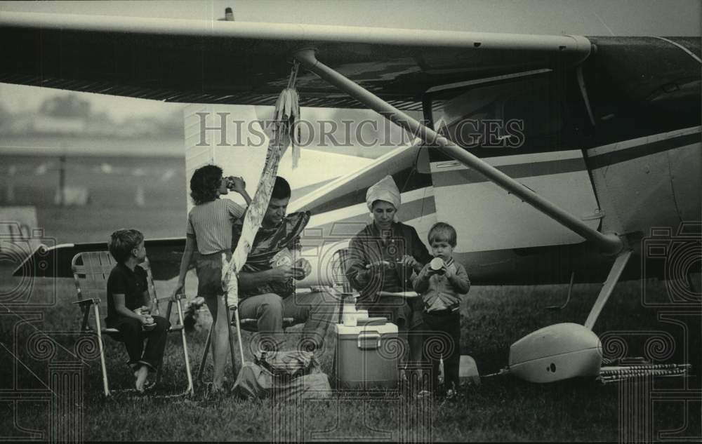 1985 Press Photo Family seeks shelter from rain under wing of plane, Oshkosh - Historic Images