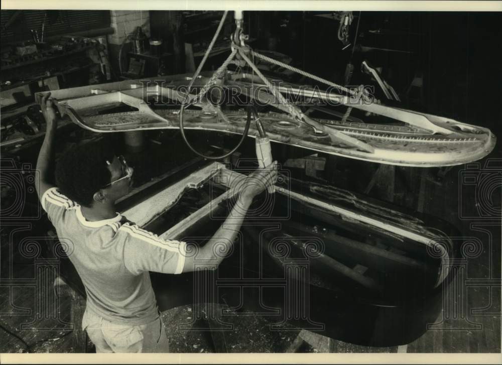 1988 Press Photo Worker lowering soundboard atop a grand piano, New York - Historic Images