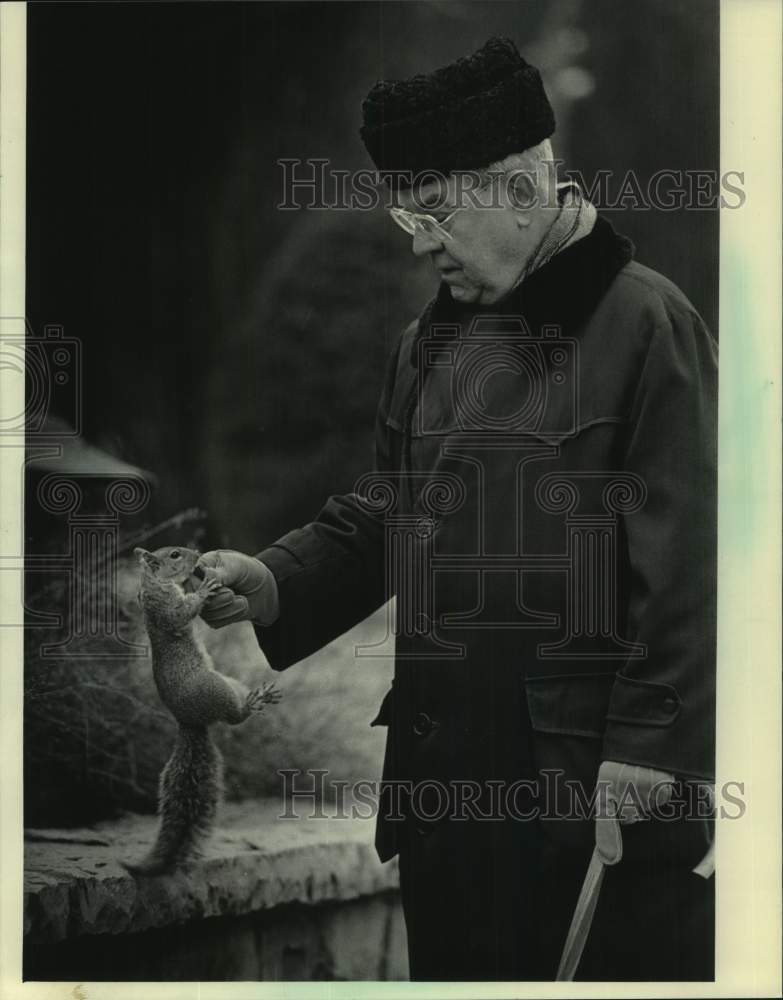 1984 Press Photo Father Thomas J. Stemper feeds a squirrel, Marquette University - Historic Images