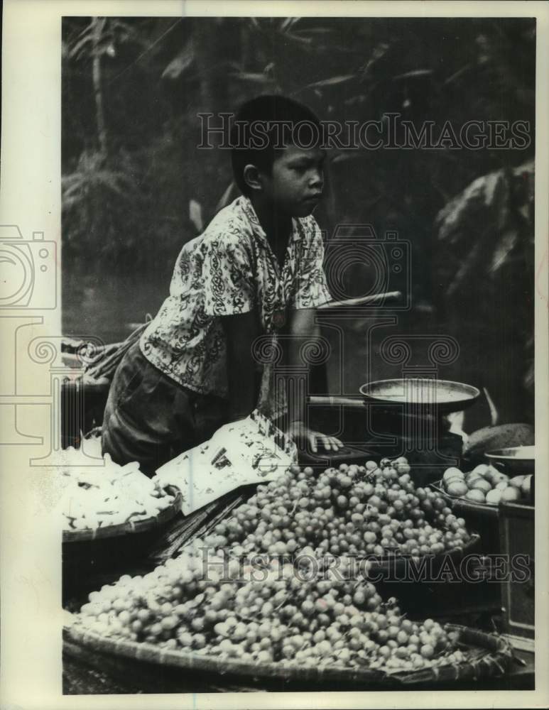 1972, A young boy looks over the fruit he hopes to sell in Thailand - Historic Images