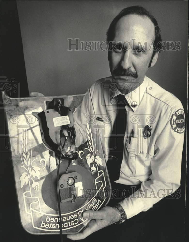 1984 Press Photo Fire inspector Karl Beaster holds melted light up beer sign, WI - Historic Images