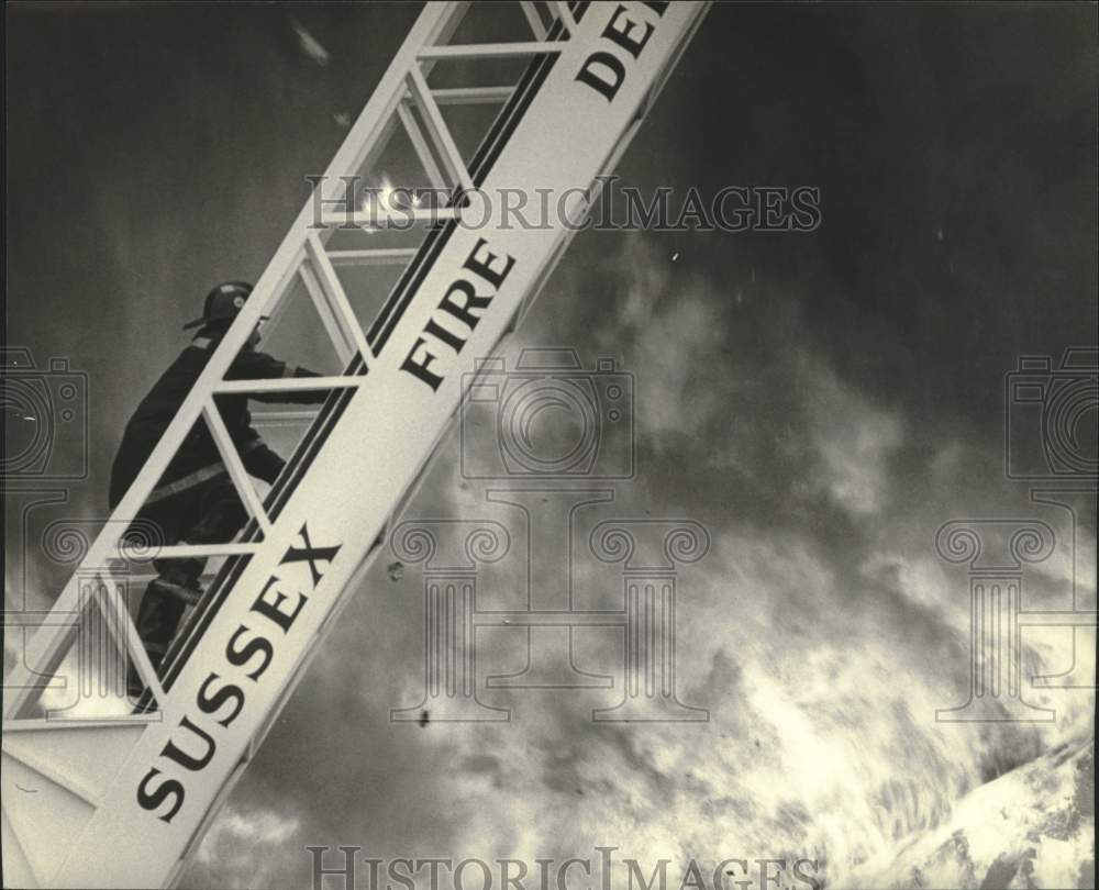 1983 Press Photo Sussex Firefighter climbing ladder in fire exercise, Muskego WI - Historic Images