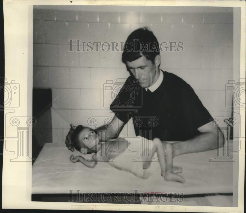 1975, Brother Regis examines a young undernourished child in Tanzania - Historic Images