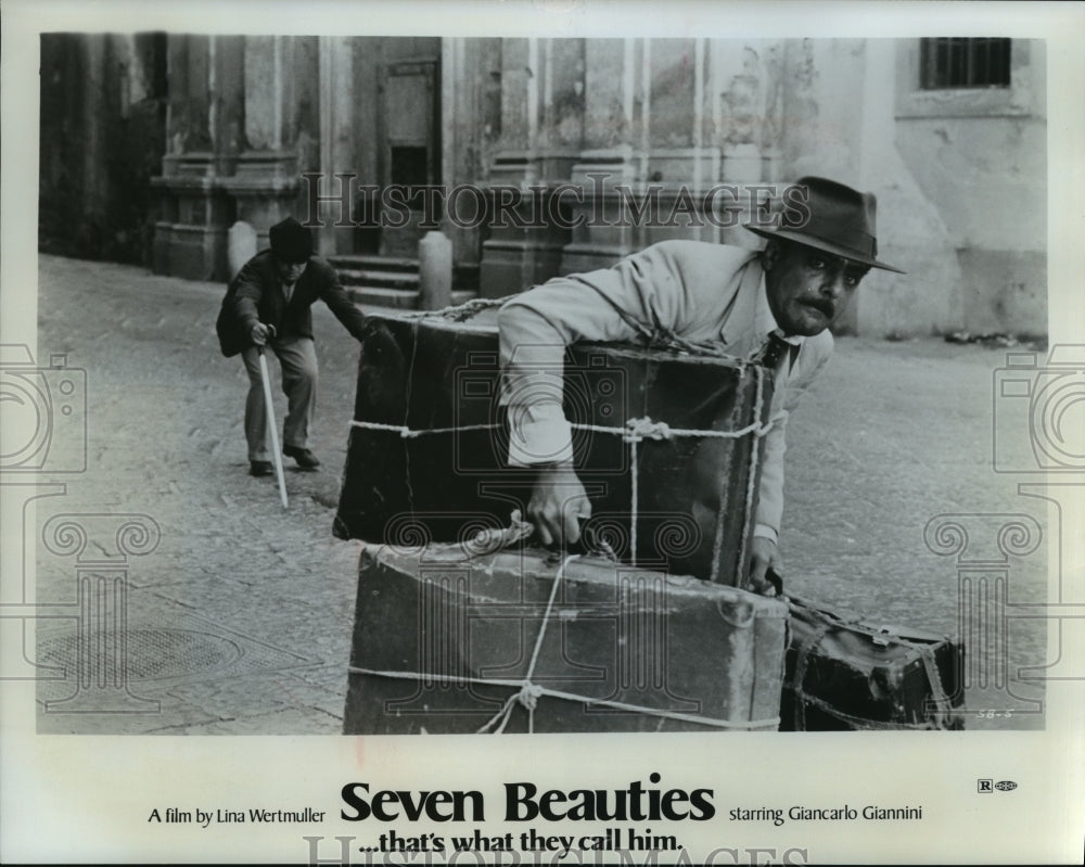 1976, Giancarlo Giannini struggling with luggage in "Seven Beauties" - Historic Images