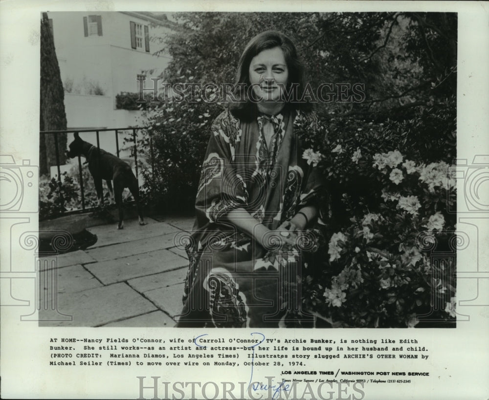 1974, Nancy Fields O'Connor, sits next to flowing bush outside home - Historic Images