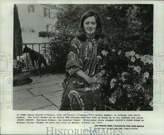 1974, Nancy Fields O'Connor, sits next to flowing bush outside home - Historic Images