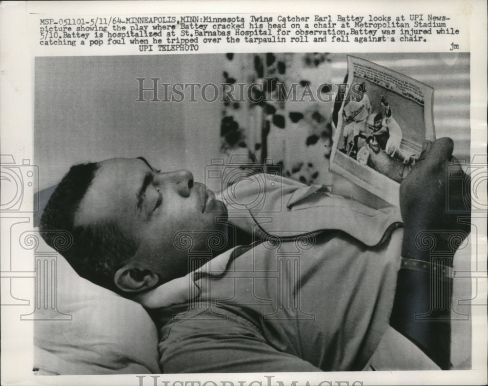 1964 Press Photo Twins catcher Earl Battey looks at UPI photo of his fall. - Historic Images