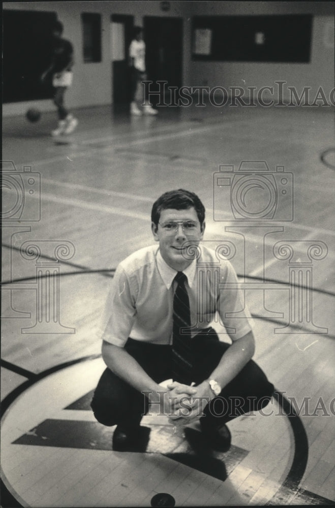 1986 Press Photo YMCA official Tom Coxey squatting on basketball court.- Historic Images