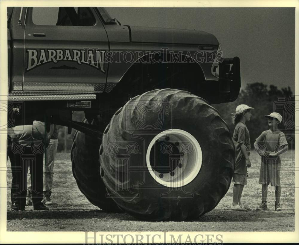 1988 Press Photo A truck with giant tires dwarfs two children in front of it- Historic Images