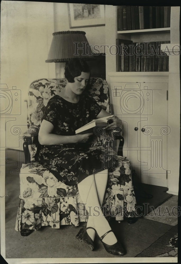 A woman sitting in a chair while reading a book  - Historic Images