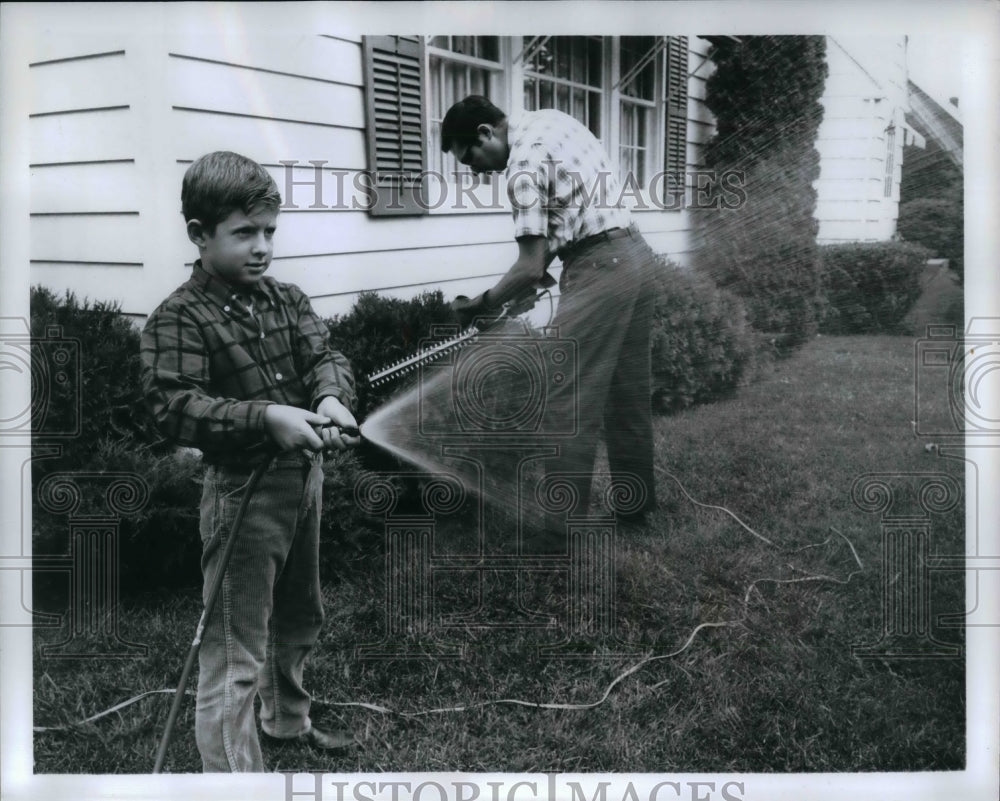 1969 Press Photo Electric hedge trimmer  in use while boy waters a lawn - Historic Images