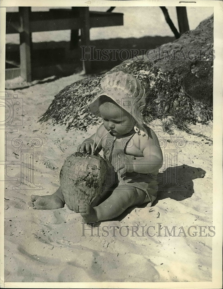 1938 tot Bonnie Dahler drinking coconut milk on the beach in Miami - Historic Images