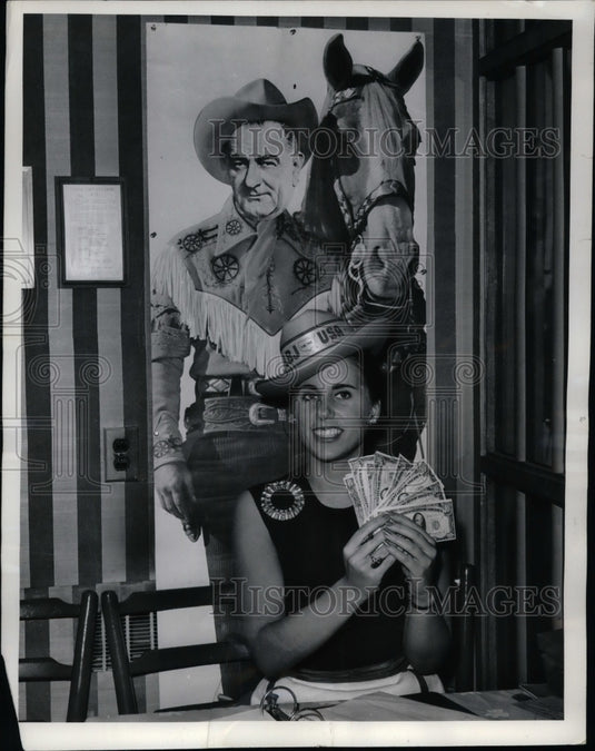 1964 Hostess Merrily Price holds bills in a new campaigning "twist" - Historic Images