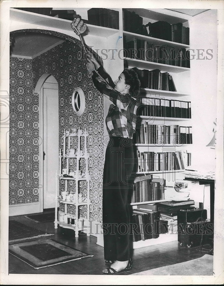 1943 A woman dusting off the bookshelf  - Historic Images