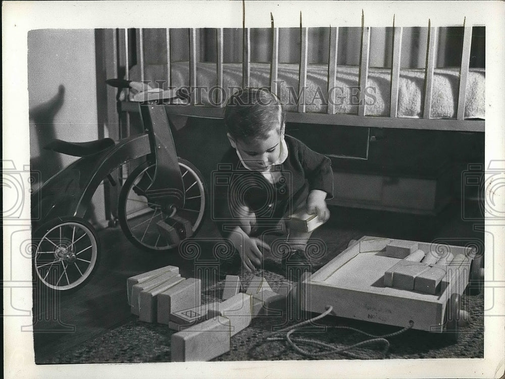 A young boy picking up his toys before going to bed  - Historic Images