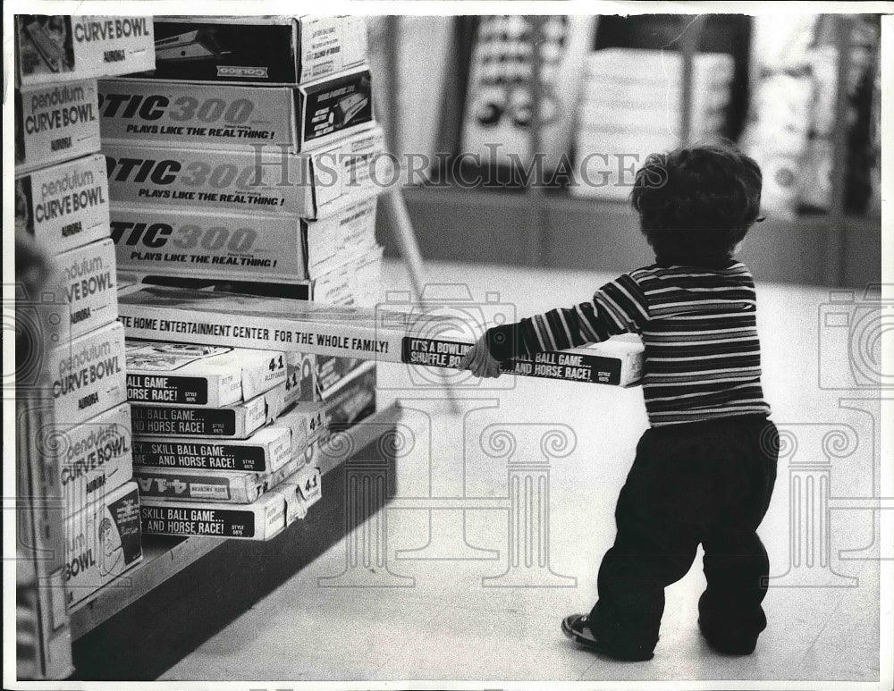 1974 Press Photo Child Pulling Out Box from Store Shelf for Christmas Shopping-Historic Images
