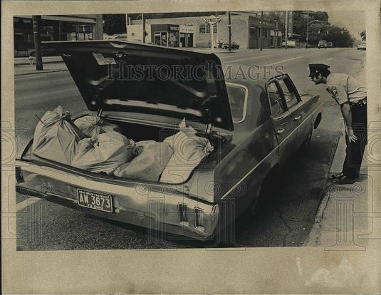 1973 Press Photo Police Officer Investigating Car with Open Trunk and Bags-Historic Images