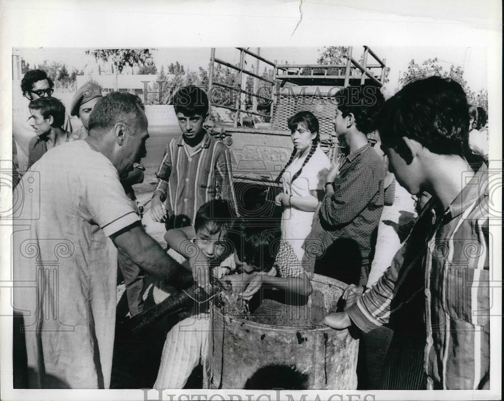 1970 Two younsters take turns being issued fresh water, Amman - Historic Images