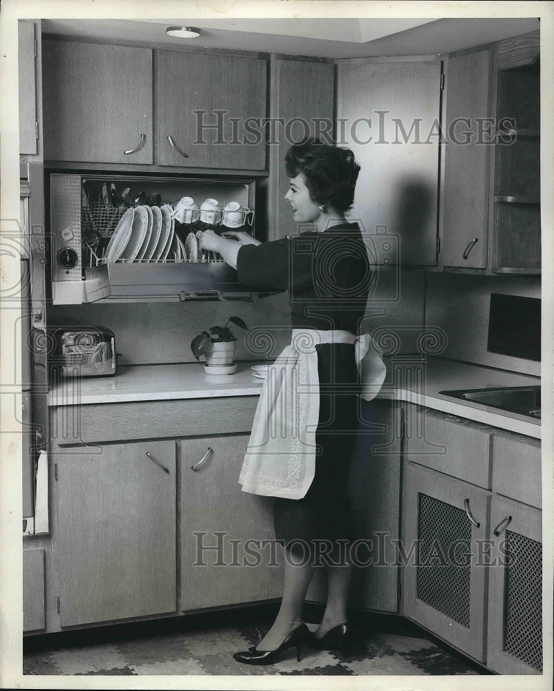 1961 A woman placing dishes in a cabinet  - Historic Images
