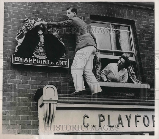 1952 Press Photo C Playford hanging a coat of arms outside of a baker's shop - Historic Images