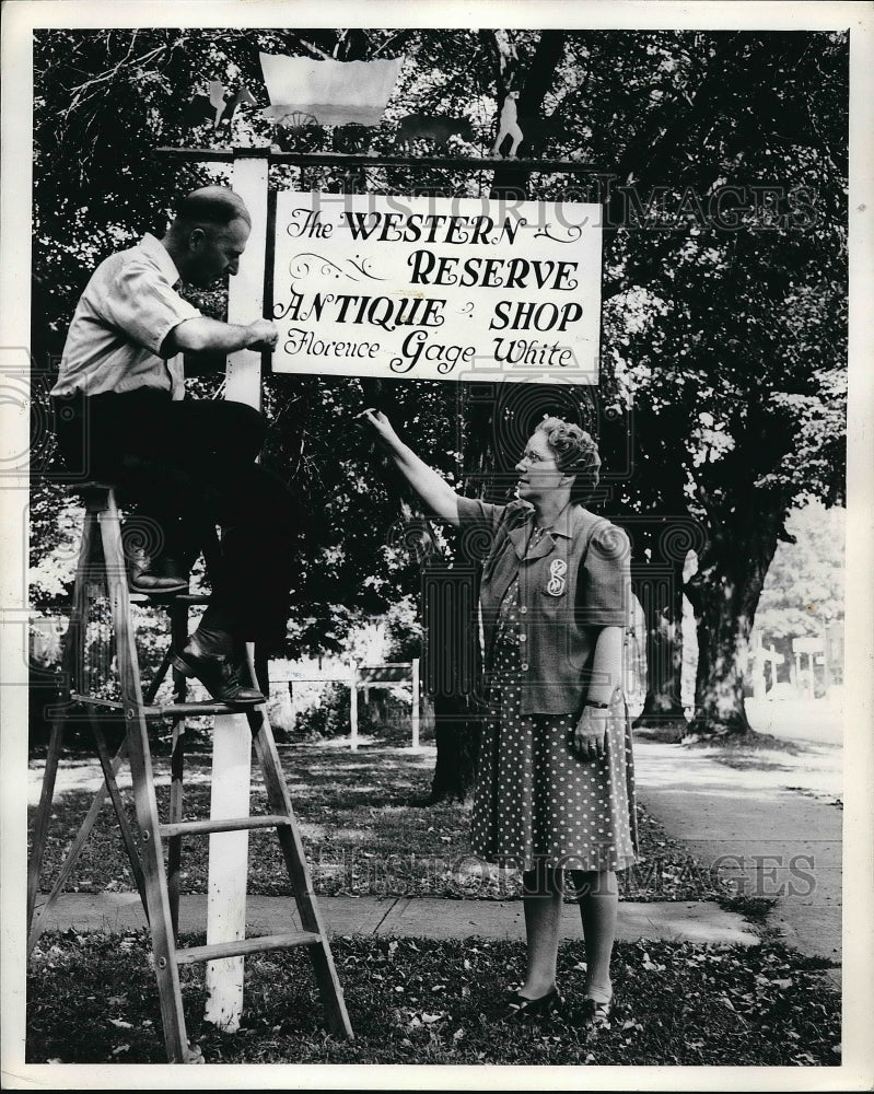 1941 Press Photo P. W. White adjust a sign for his wife at her antique shop-Historic Images