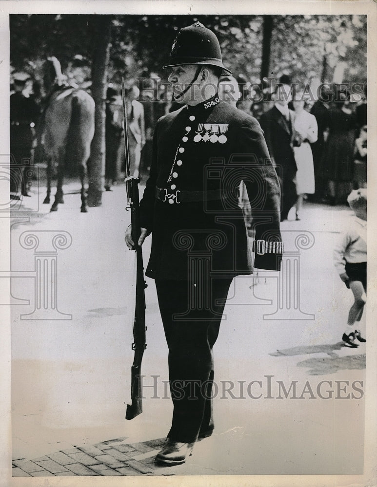 1939 Press Photo London policeman carries rifle of guardsman who fainted in heat-Historic Images