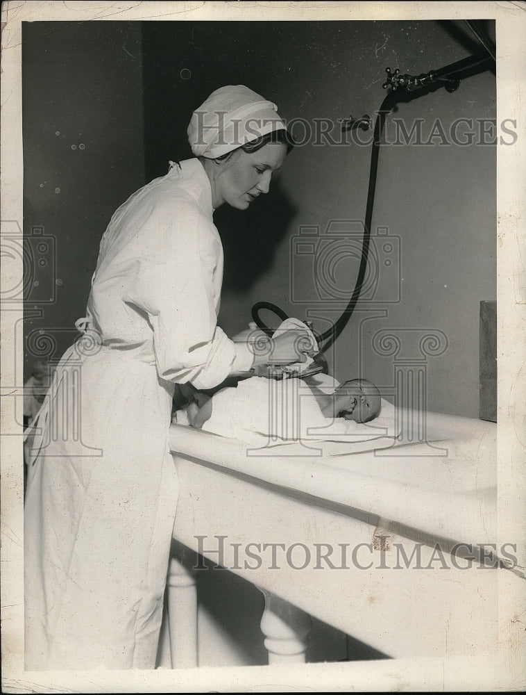 1934 Loyola Kapel, nurse changes baby in hospital nursery - Historic Images