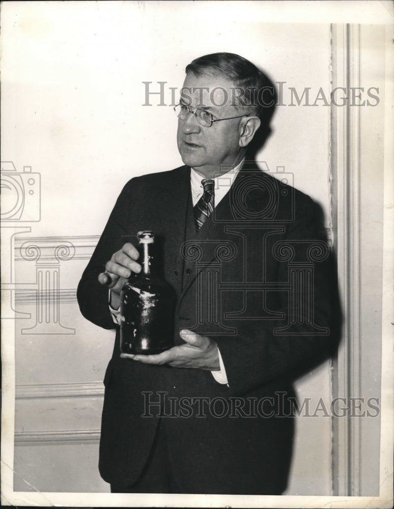 1935 Secretary of Interior holding a found bottle of rum - Historic Images