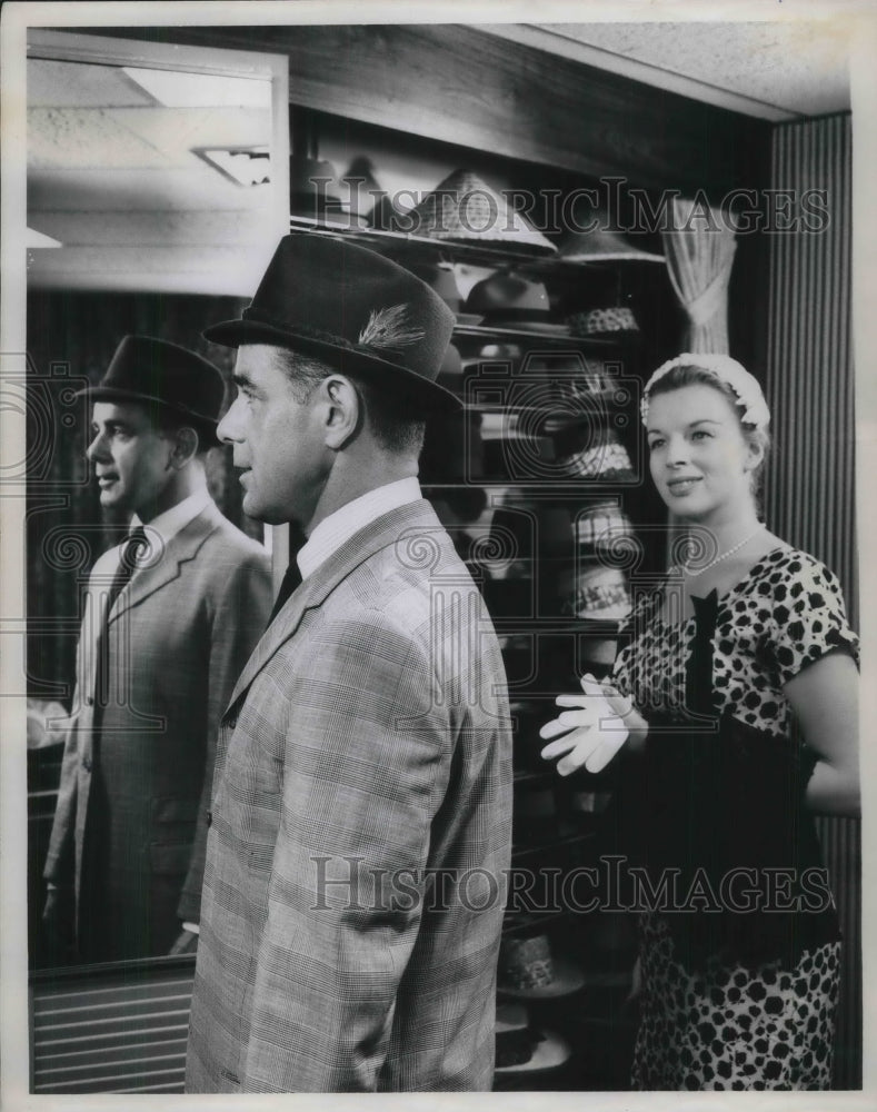 1960 man trying on a hat while lady looks on approvingly - Historic Images