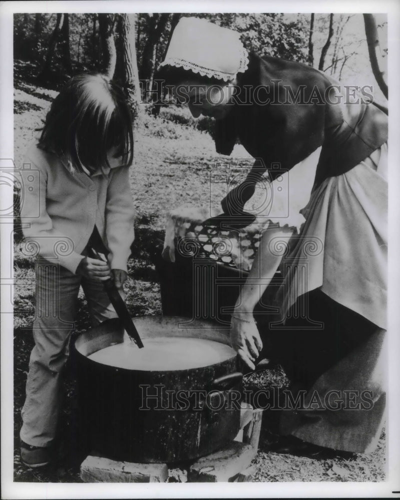 Press Photo Lady with a Young Girl Stirring a Pot on Outside Fire - Historic Images