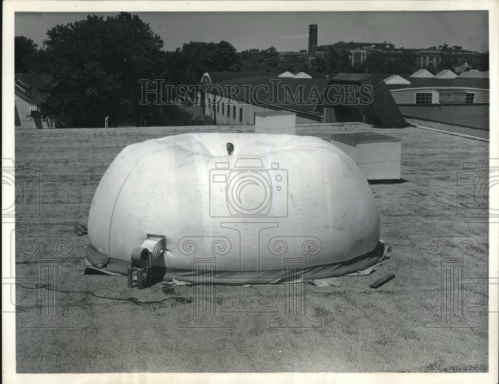 1958 Press Photo Man Rides Comfortably on Giant White Blob On Top Of Building - Historic Images