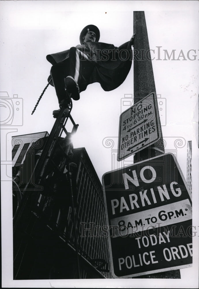 1970 Carmen Pastor on signpost waits to see parade on his unicycle - Historic Images