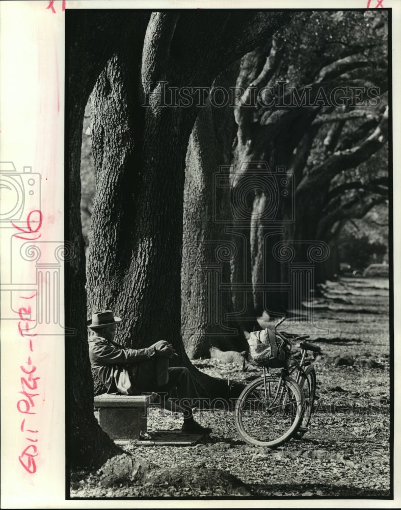 1985 Press Photo Man Sitting On Bench Among Trees Next To Bike - Historic Images