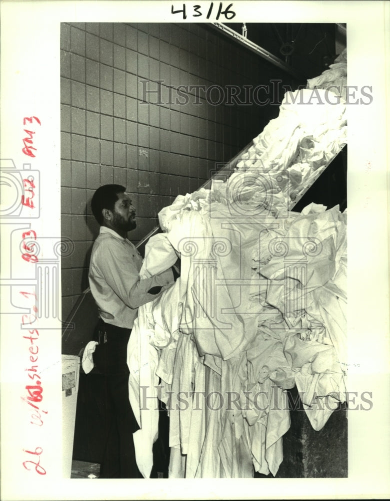 1986 Press Photo Henry Polk loads conveyor belt with laundry from area hospitals - Historic Images