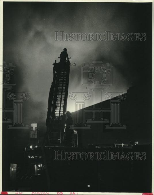 1986 Press Photo Night view of a fireman on the ladder fighting fire. - Historic Images