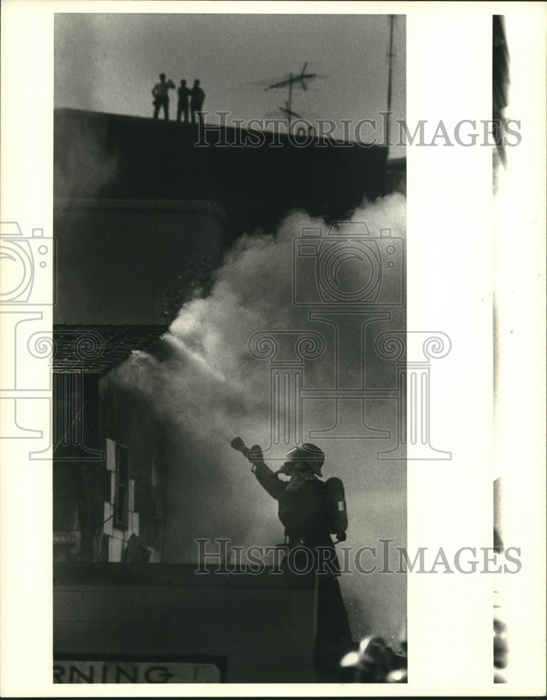 1988 Press Photo Firemen battle blaze as spectators watch from roof in back. - Historic Images