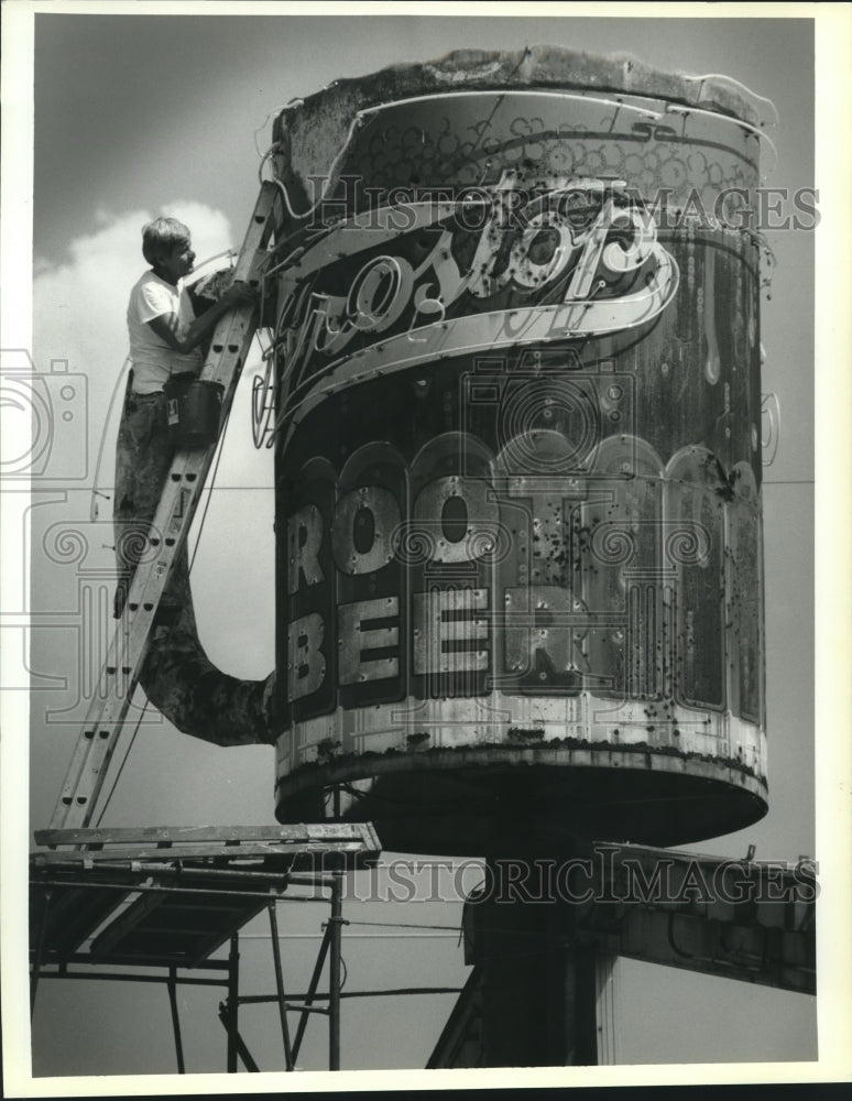 1991 Press Photo Curtis Richardson paints the rusty old mug atop Frostop Burger - Historic Images