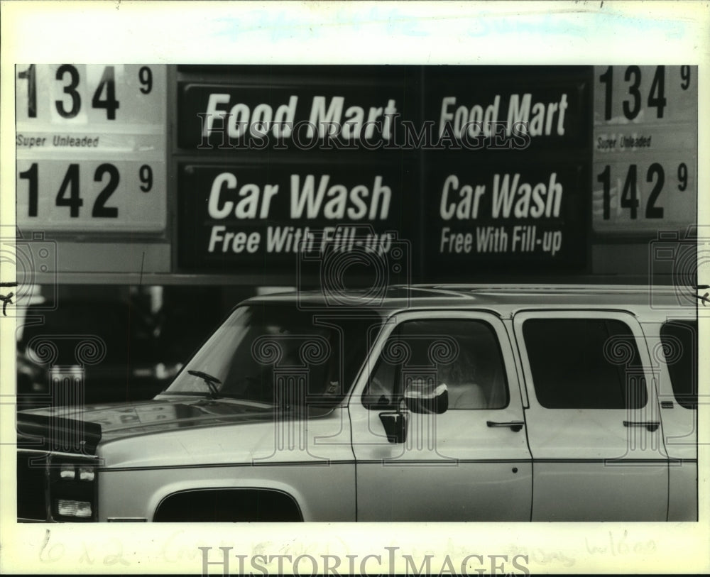 1990 Press Photo A woman driving a truck drives past higher gas prices. - Historic Images