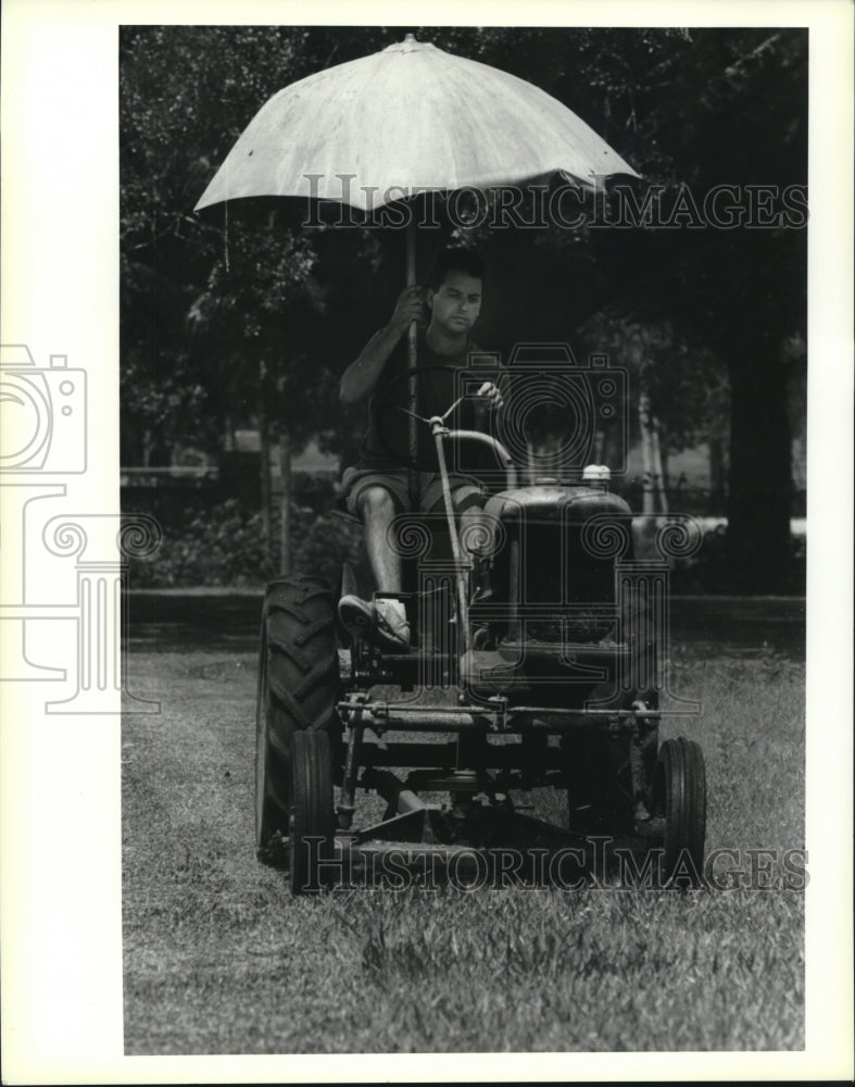 1995 Press Photo Peter Foles cuts grass while holding umbrella, Violet - Historic Images