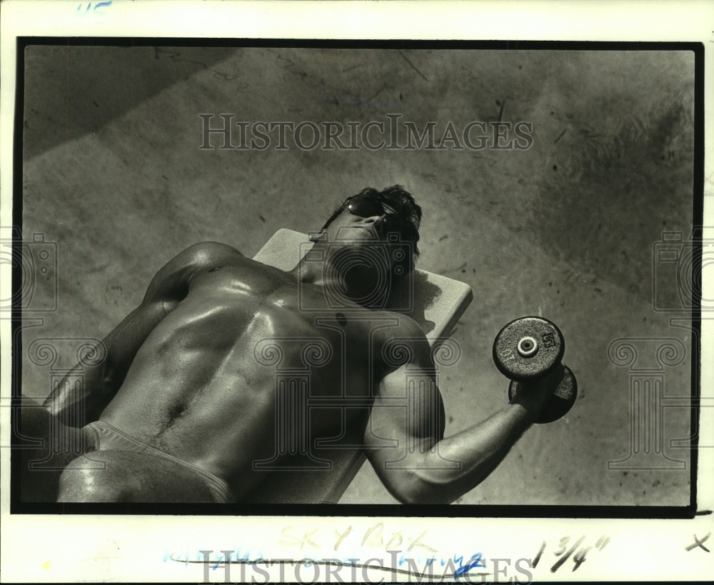 1986 Press Photo Augie Guillot catches some rays poolside while weightlifting - Historic Images