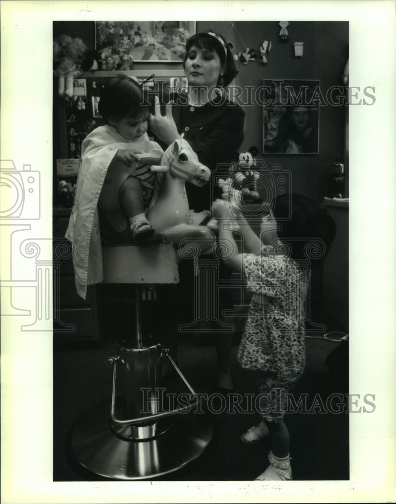 1994 Press Photo Allison Eckert sits on toy horse as Kathy Medina cuts her hair. - Historic Images